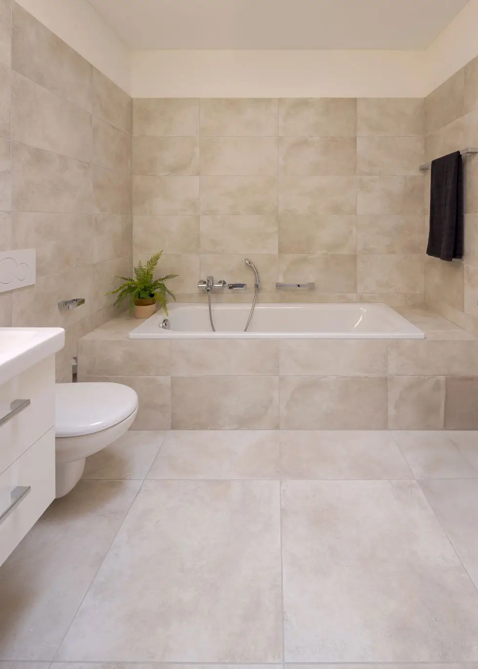 Modernes Badezimmer mit Badewanne, Toilette, Waschtisch und hängender schwarzer Lampe mit goldfarbenem Inneren.