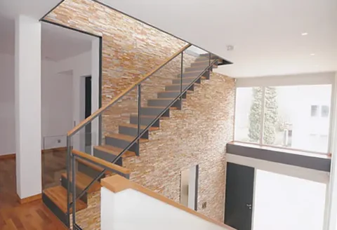 Moderner Innenraum mit Treppe, Holzgeländer und Wand aus Naturstein.