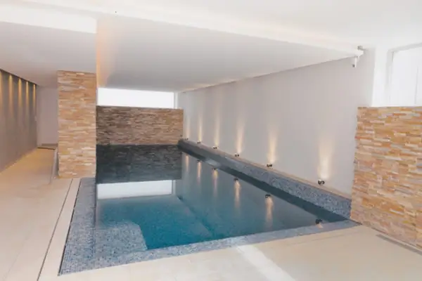 Innenraum mit rechteckigem Schwimmbecken, weißen Wänden und Wandverkleidungen aus hellem Naturstein.