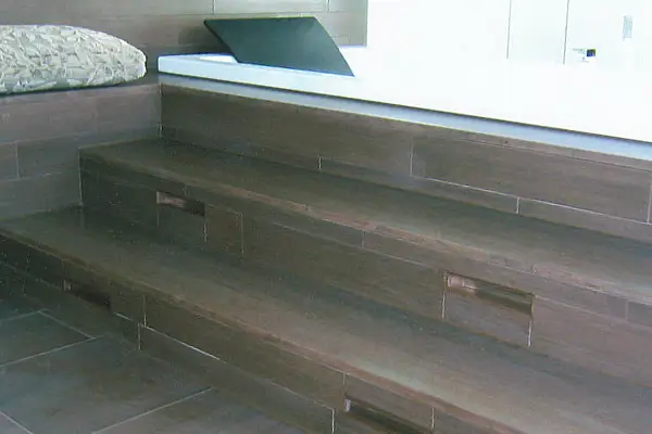 Treppenstufen aus Naturstein mit eingelassenen Griffmulden neben einem Fenster und einem Kissen auf der Fensterbank.