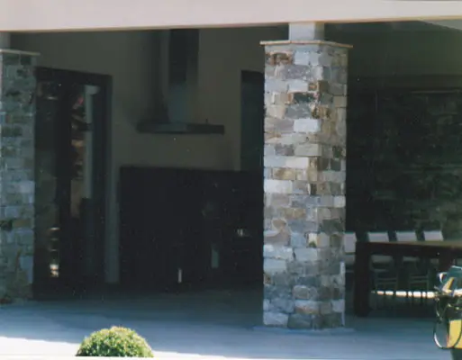 Zwei massive Säulen aus Naturstein vor einem dunklen Innenraum mit sichtbarem Esstisch und Stühlen.