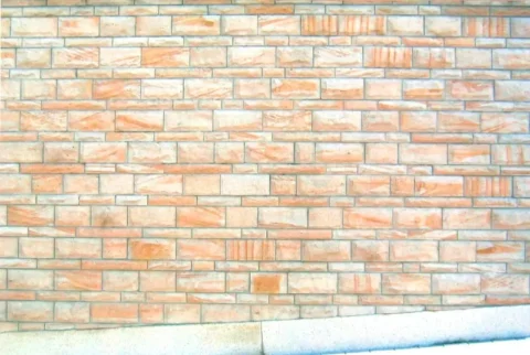 Mauer aus rechteckigen, unterschiedlich großen Ziegelsteinen mit sichtbarem Mörtel und einem Betonabsatz am unteren Rand.
