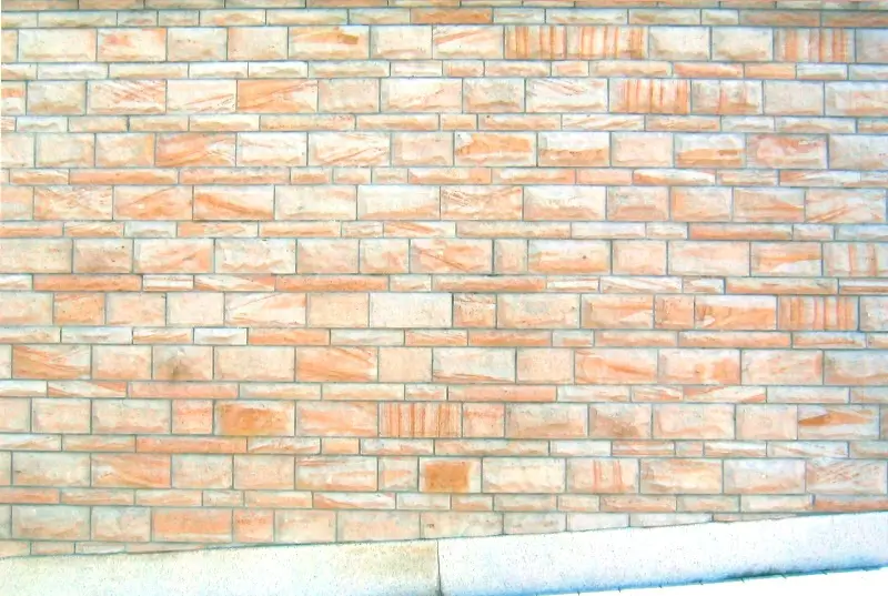 Mauer aus rechteckigen, unterschiedlich großen Ziegelsteinen mit sichtbarem Mörtel und einem Betonabsatz am unteren Rand.