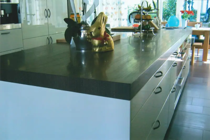 Kücheninsel mit dunkler Arbeitsplatte, darauf zwei Schokoladenhasen und ein mehrstöckiges Metallgestell mit Obst und Blumen im Hintergrund.